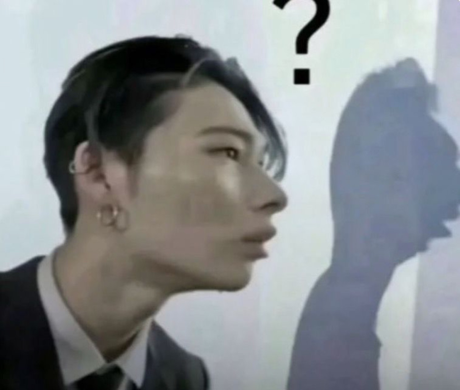 Young Asian man in profile glancing at a shadow with a question mark floating above his head
