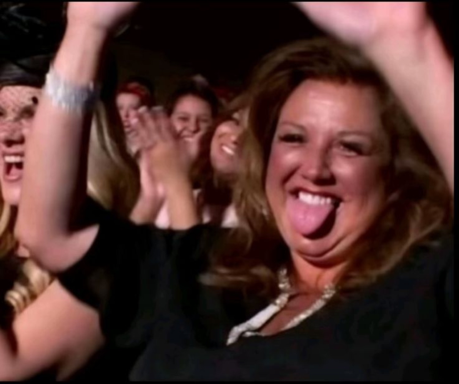 Woman in a crowd throwing her arms up and sticking her tongue out in celebration
