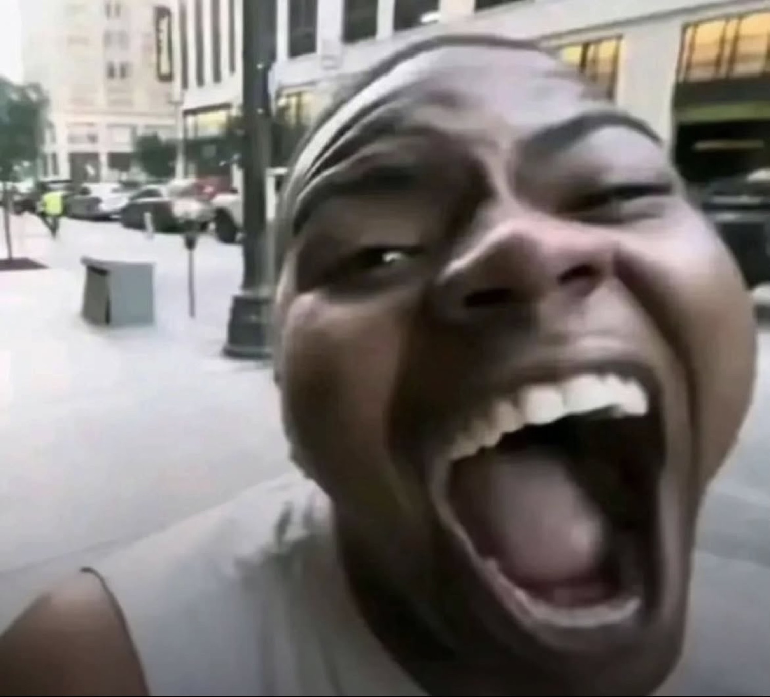 Man leaning into the camera on a city sidewalk, mouth wide open mid-scream