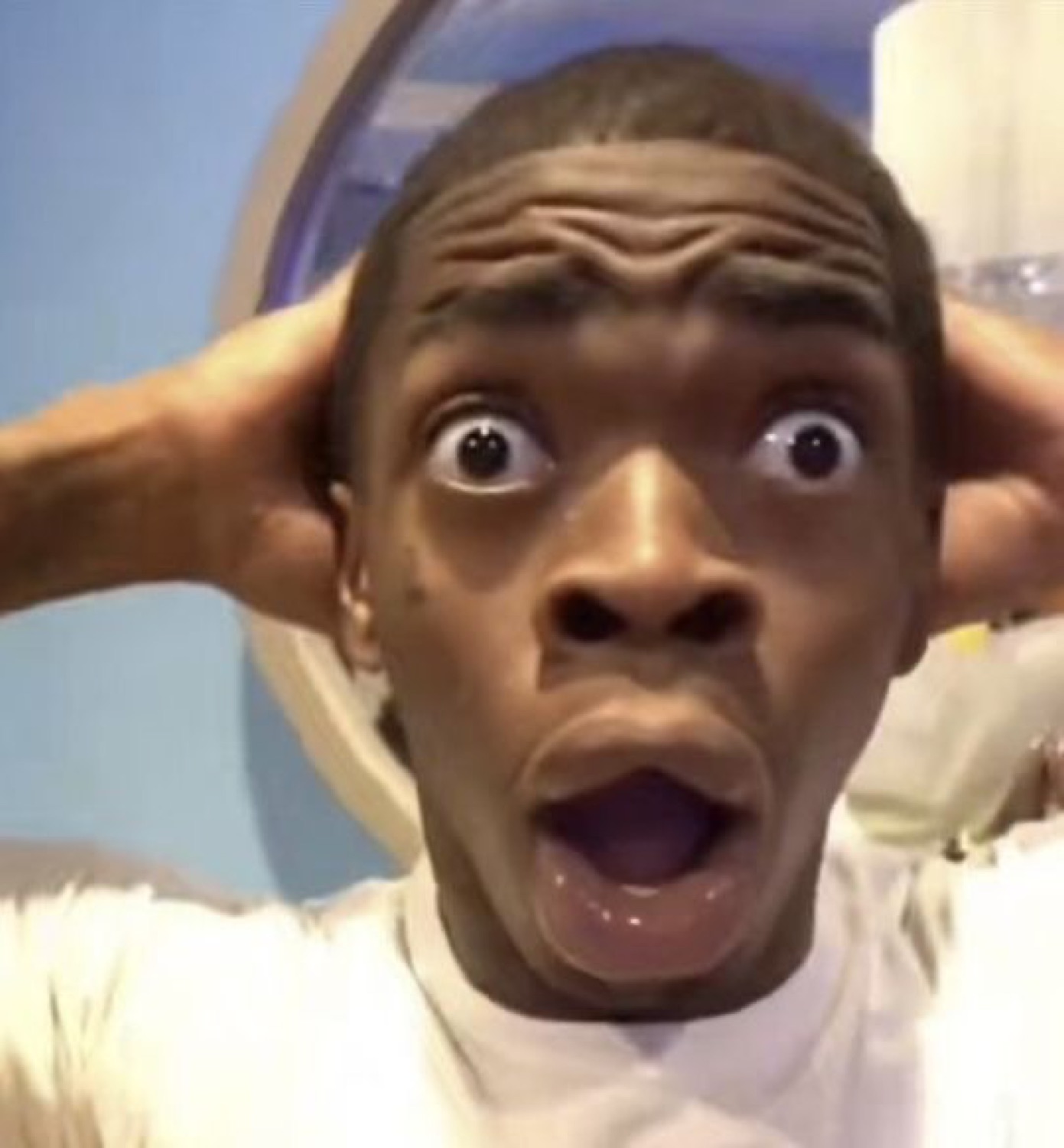 Young man clutching his head with both hands, mouth wide open in total shock