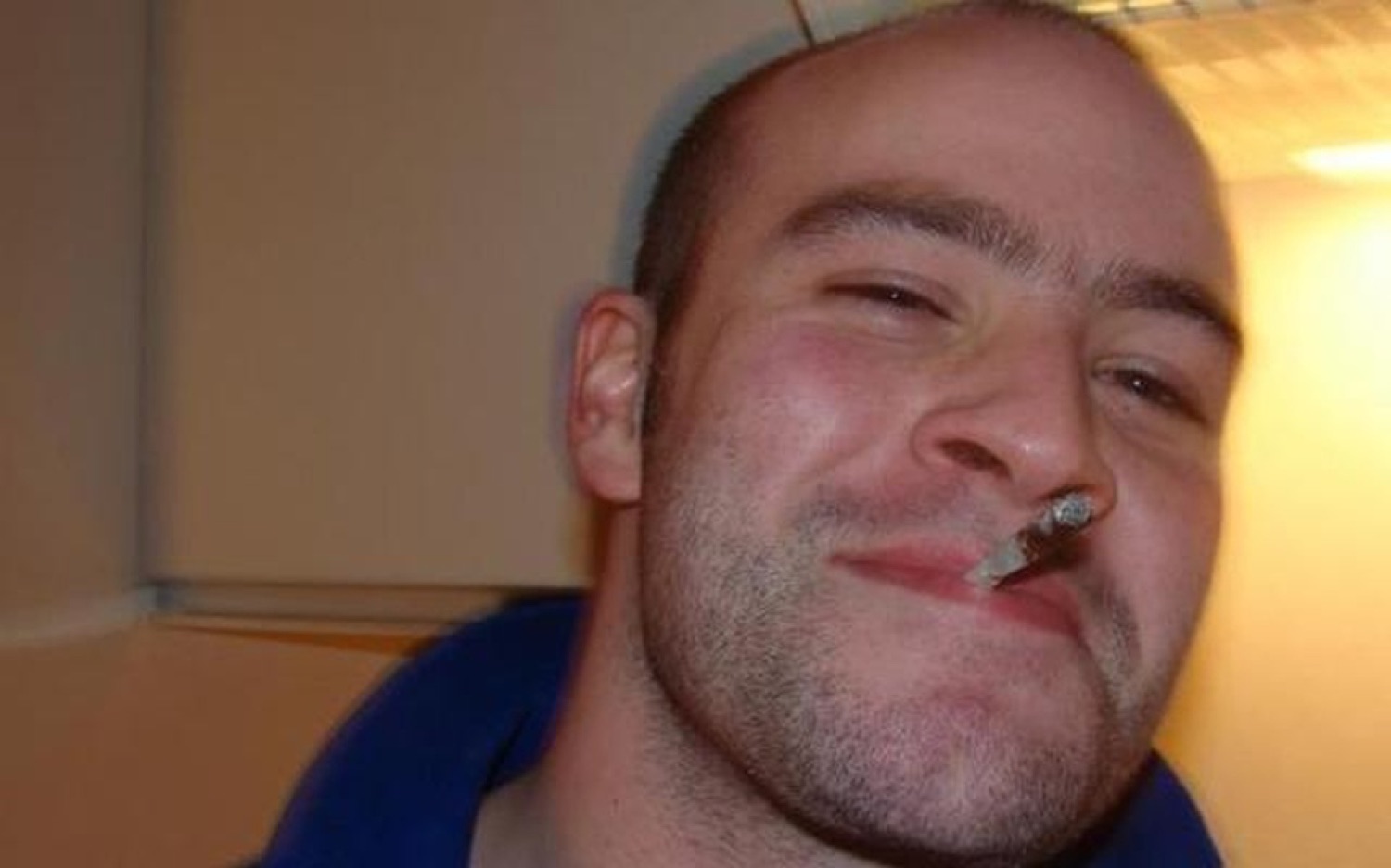 Bald guy squinting with a cigarette hanging from his lip and a self-satisfied grin