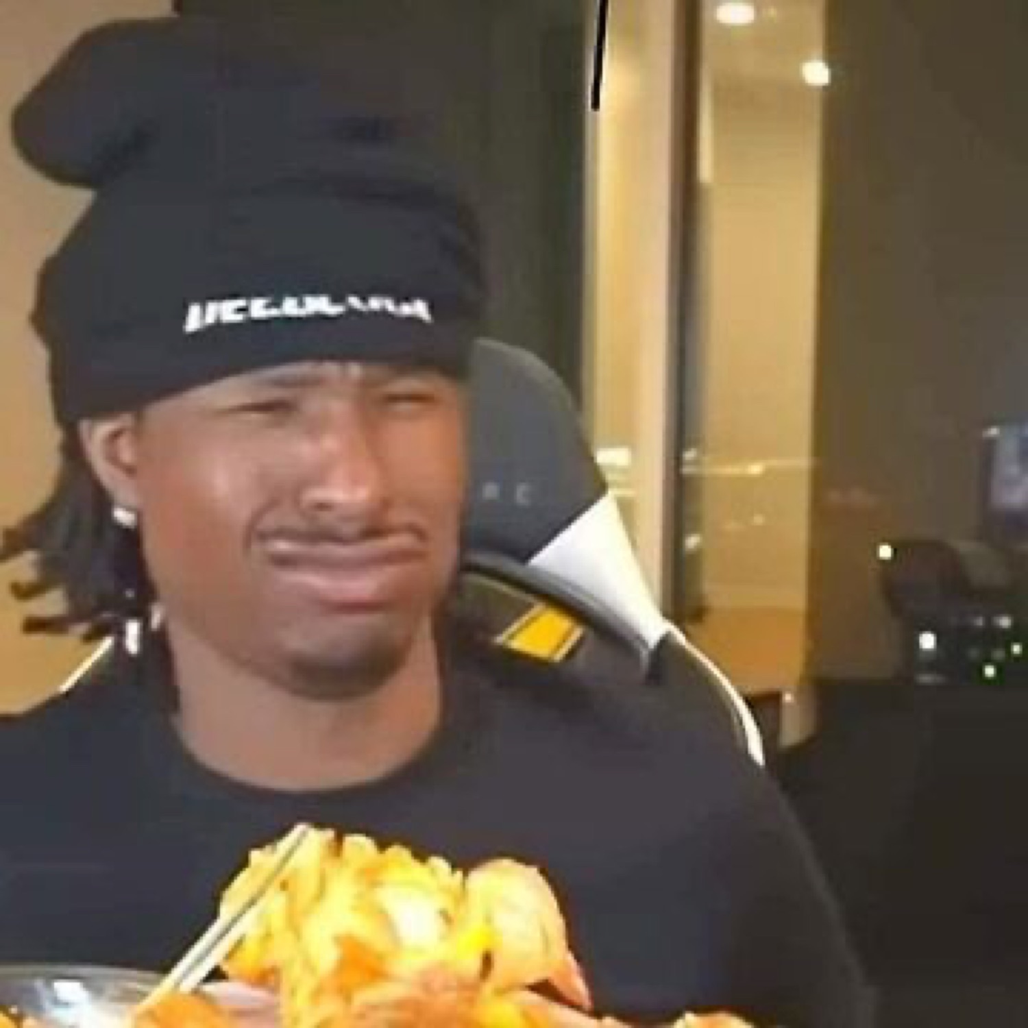 Guy in a black beanie crying while holding chopsticks over a plate of food