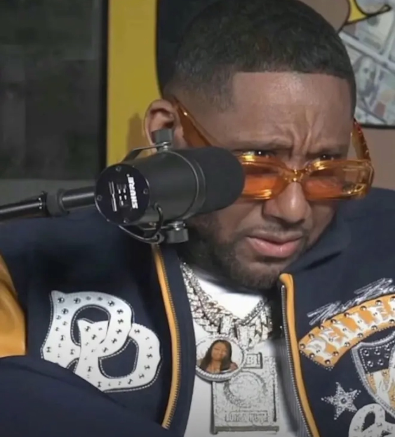 Man in orange shades at a podcast mic squinting in disgust