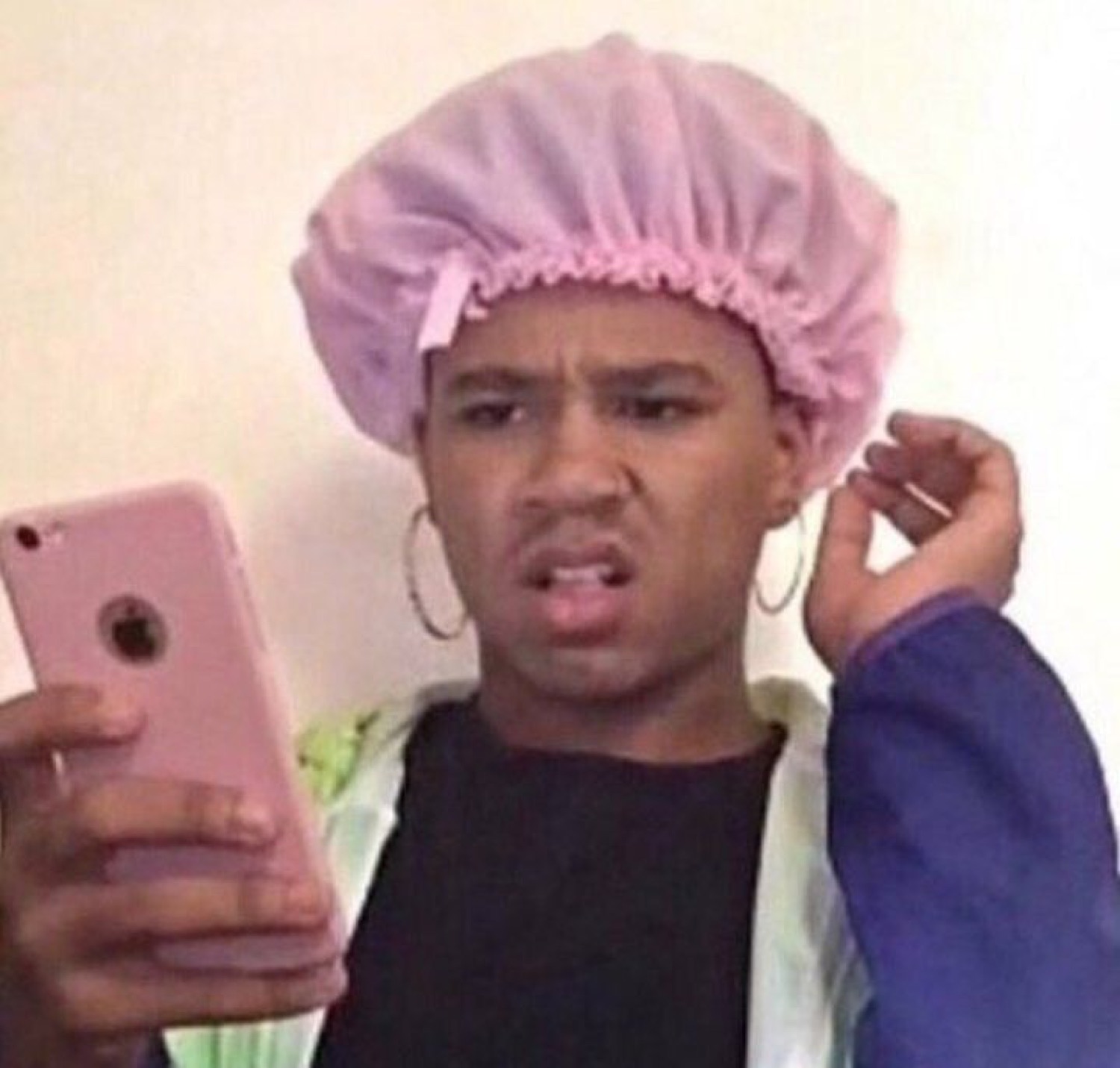 Guy in a pink bonnet and hoop earrings holding a phone with an annoyed, judgy scowl