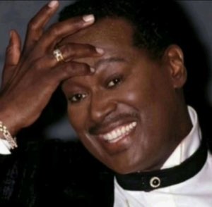 Man laughing hard with hand pressed to his forehead and a gold ring glinting