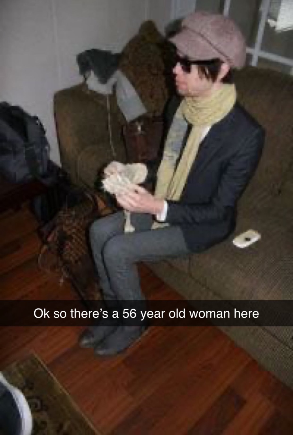 Man in a newsboy cap and sunglasses sitting on a couch with the 'Ok so there's a 56 year old woman here' caption