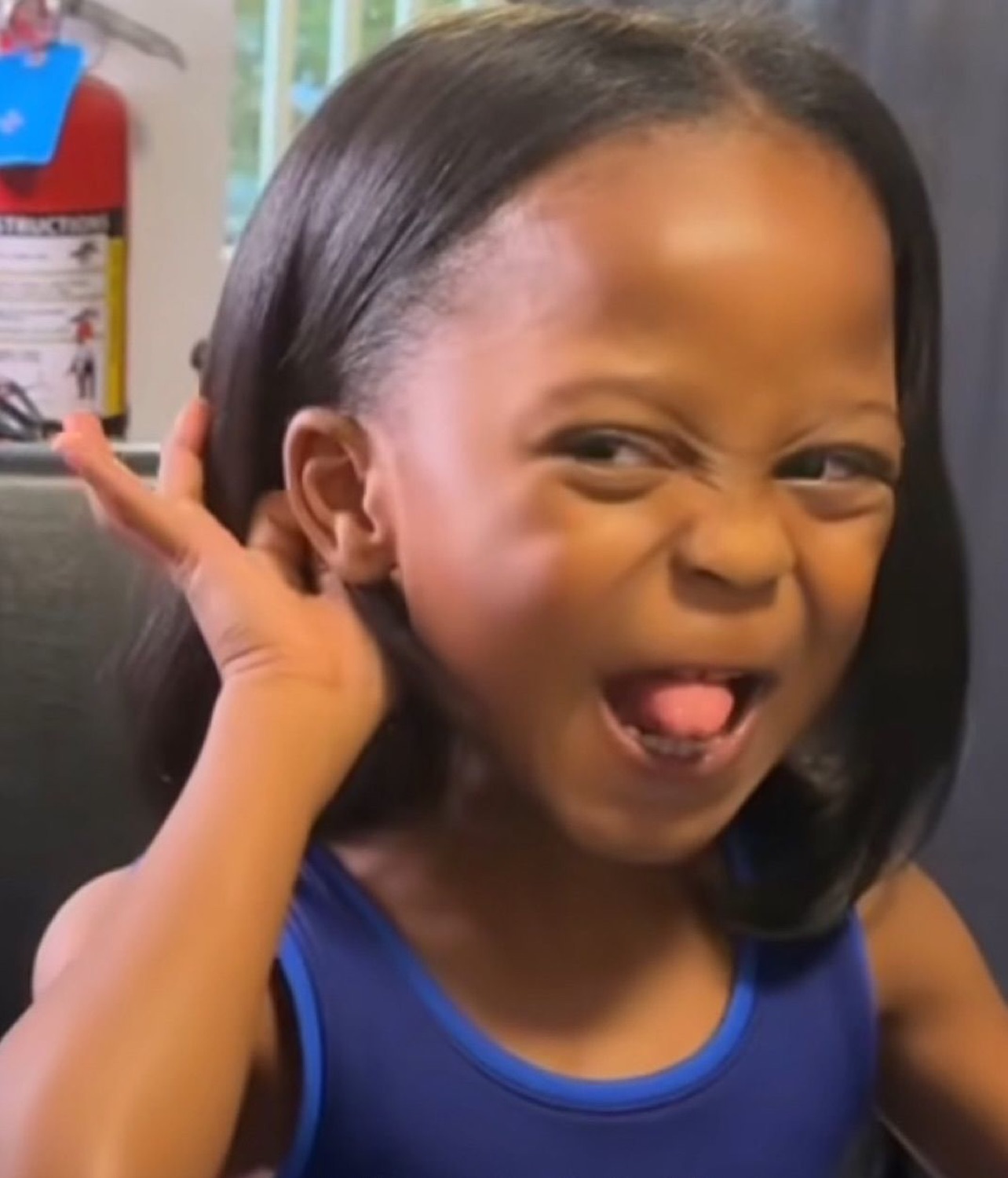 Young girl squinting and sticking her tongue out with hand raised to ear, utterly unbothered