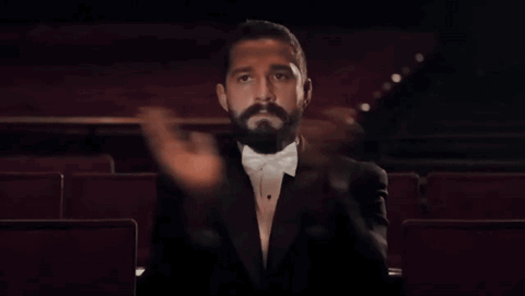 Bearded man alone in a dark theater slowly clapping