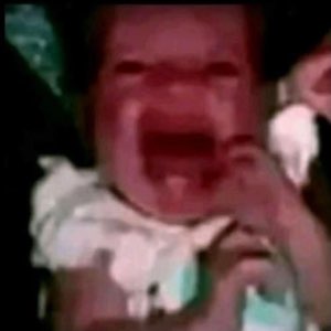 Grainy dark photo of a red-faced baby screaming and crying with its mouth wide open