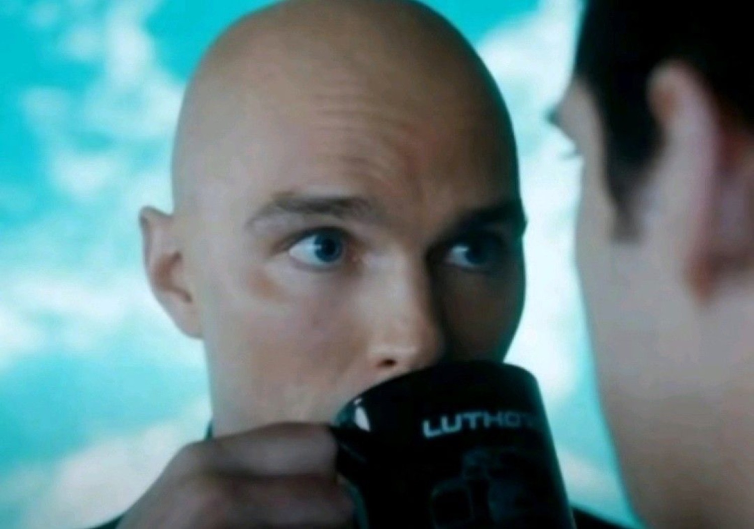 Bald man sipping from a 'LUTHOR' mug while eyeing someone with wary suspicion