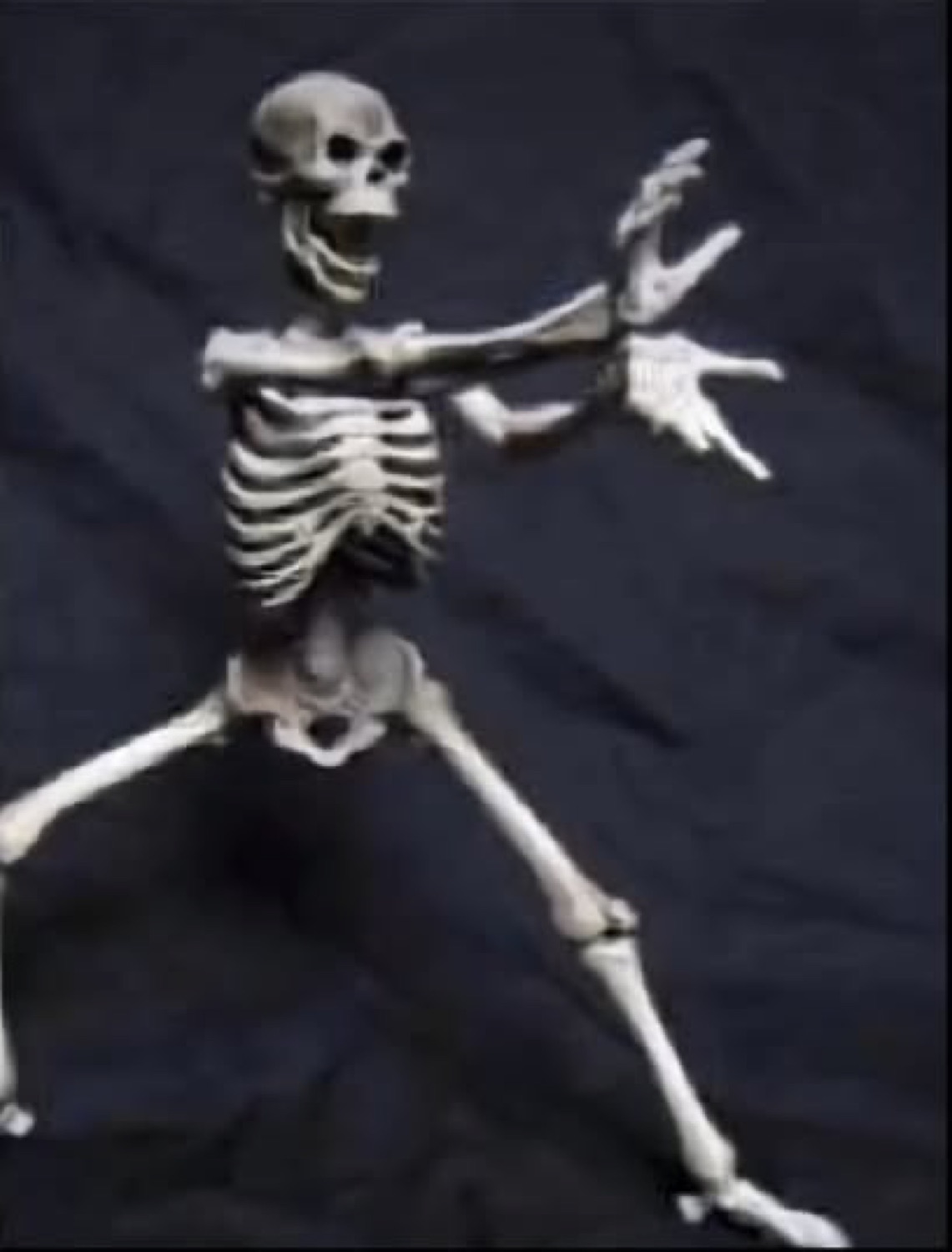 Grinning skeleton dancing with its arms flung out on a dark background