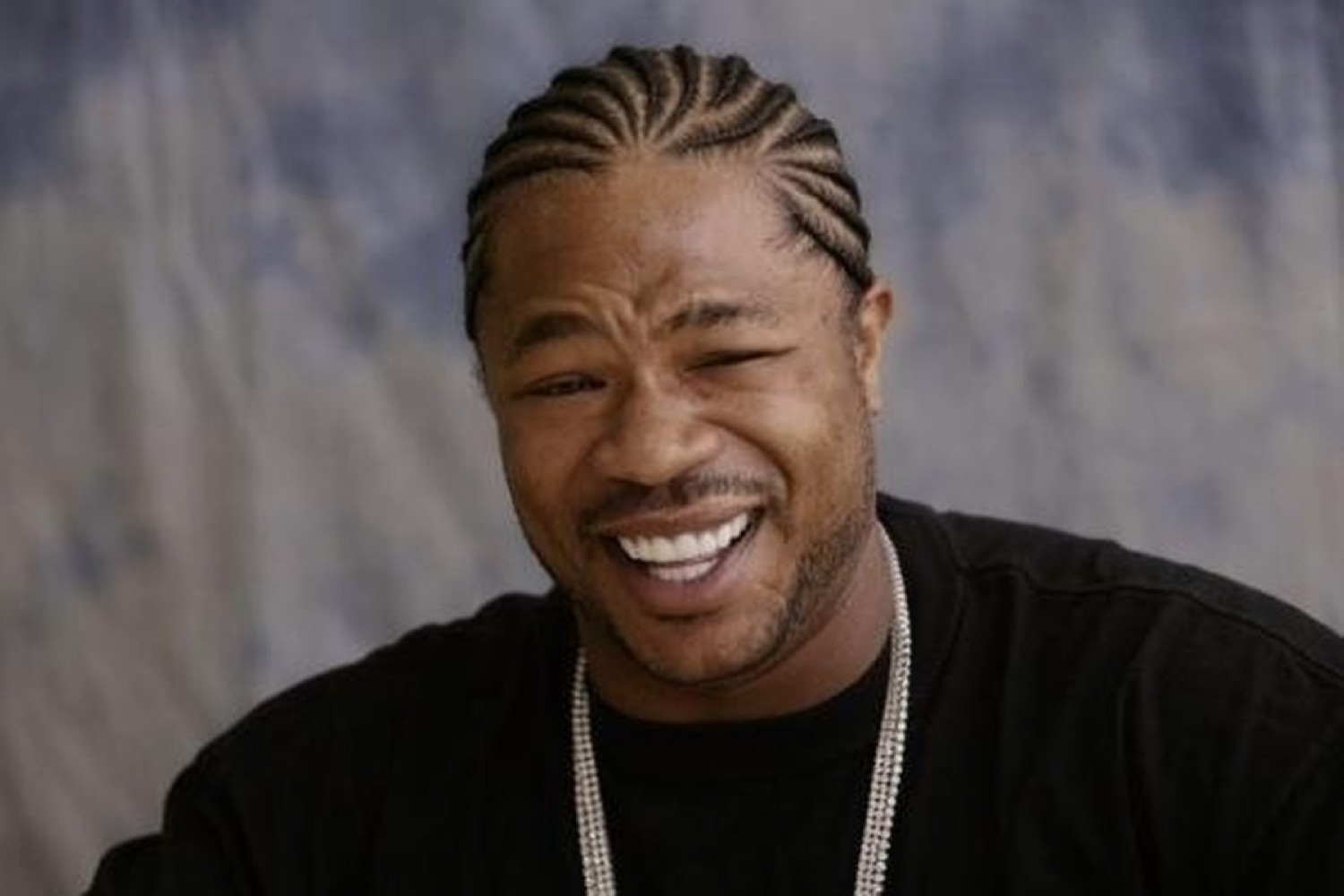 Xzibit cracking up laughing in a black shirt with a silver chain, pure joy on his face