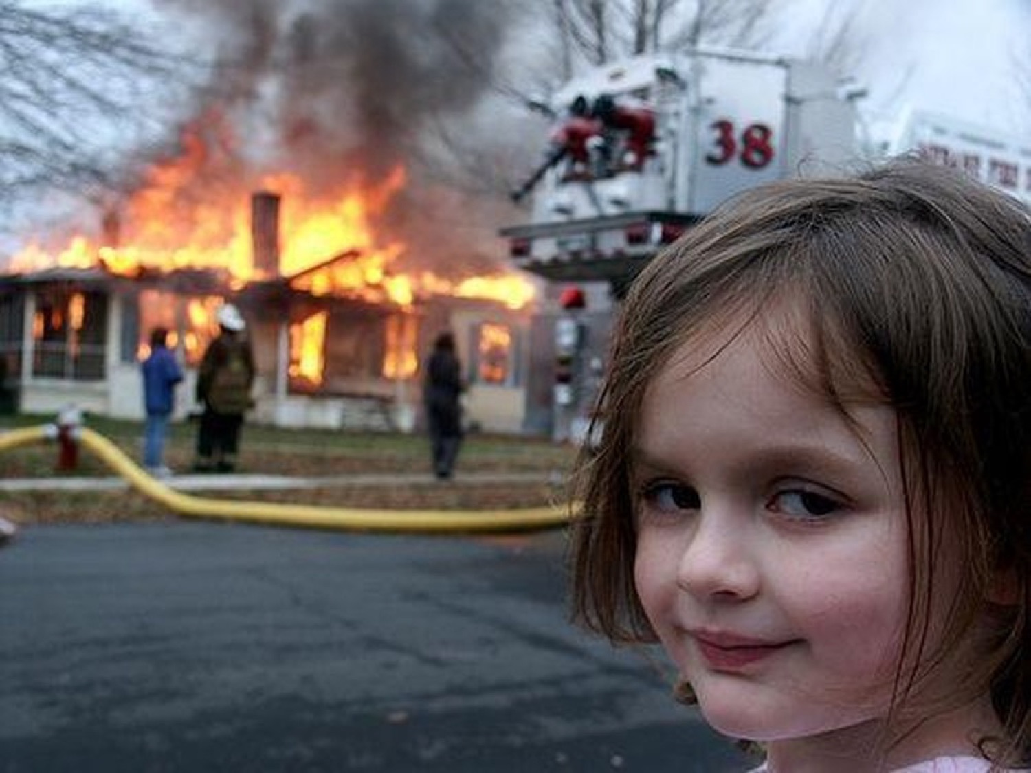 The Disaster Girl smirking slyly at the camera as a house burns behind her