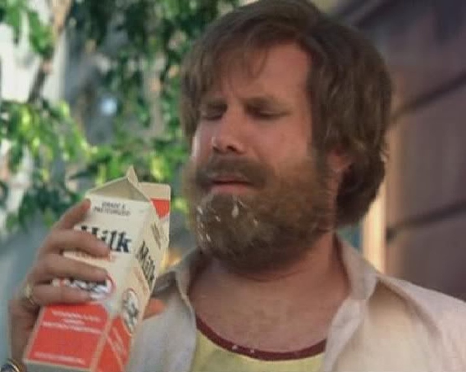 Bearded man eyeing a carton of milk with a weary, unimpressed frown
