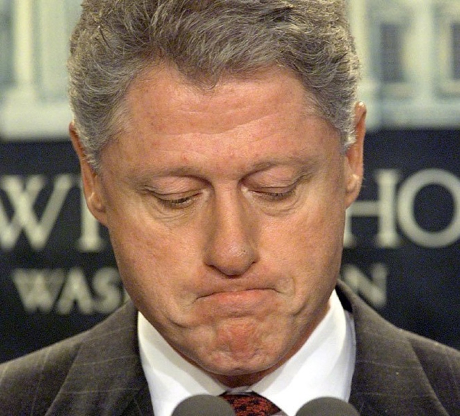 Bill Clinton at a podium looking down with a pained, lips-pressed grimace
