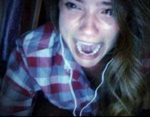 Girl on a webcam screaming in terror with eyes wide in a dark room