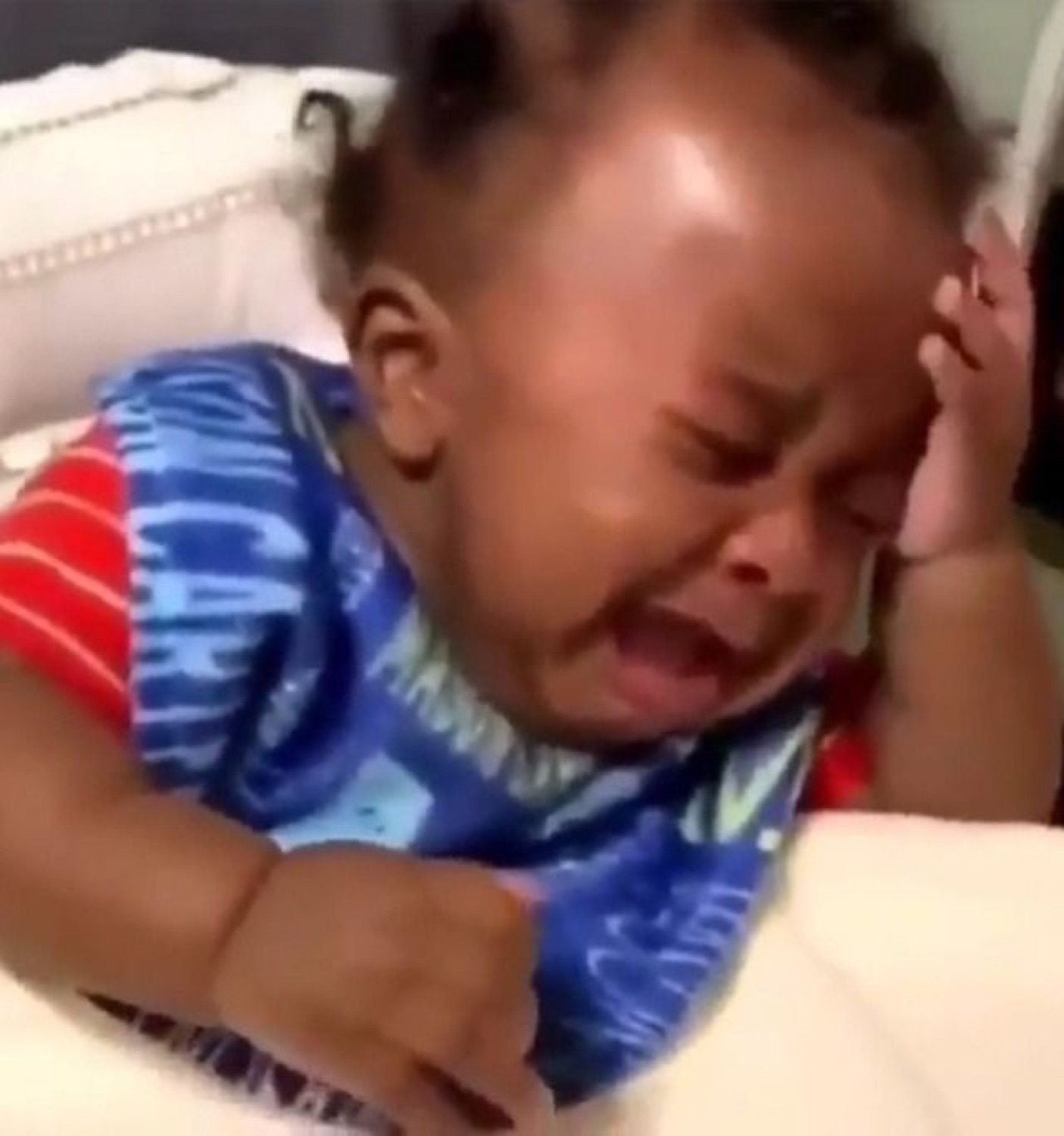 Baby in a blue onesie crying hard with scrunched face and fist clenched