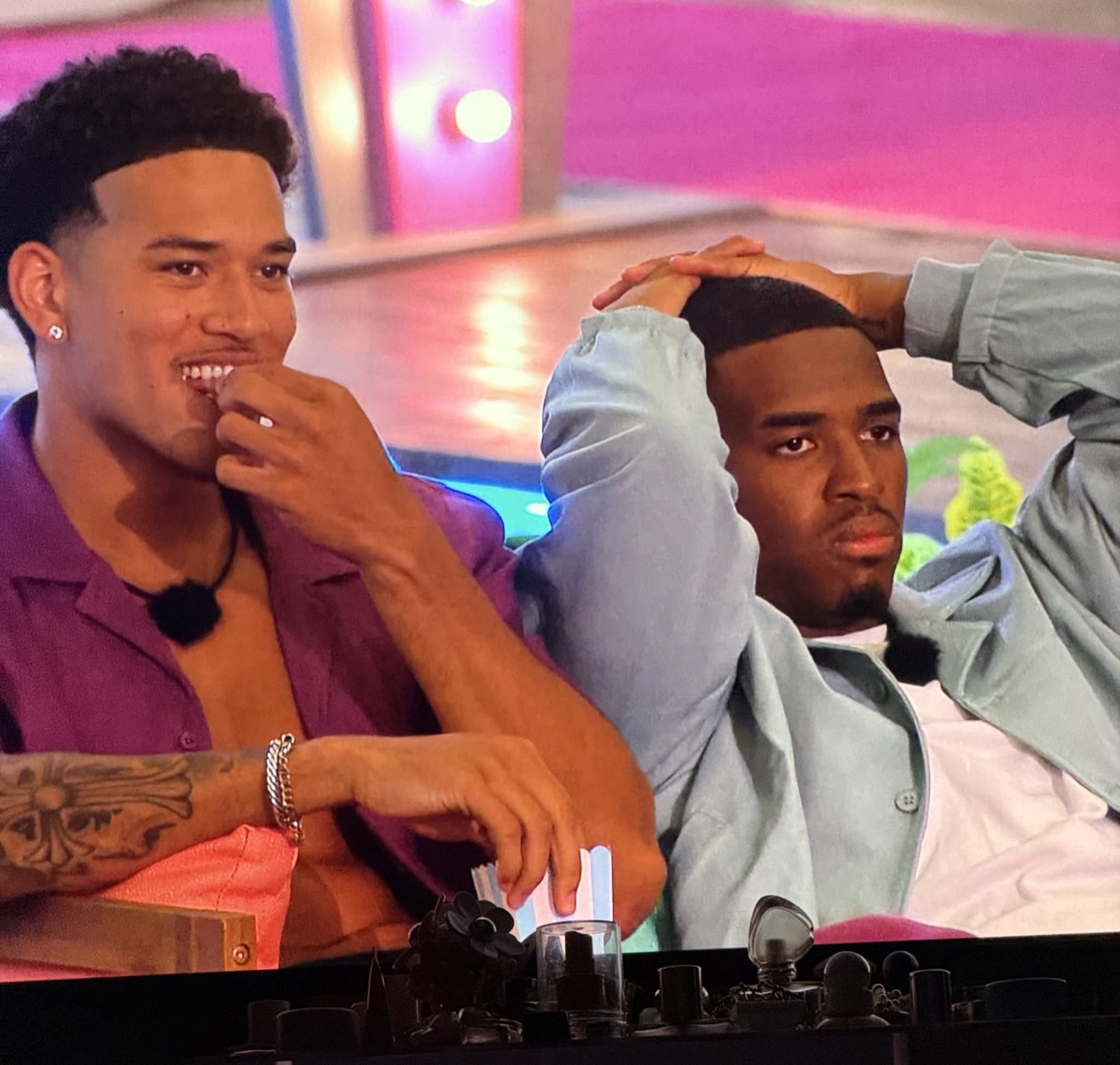 Love Island USA's Corbin grinning behind his hand while another islander clutches his head in disbelief