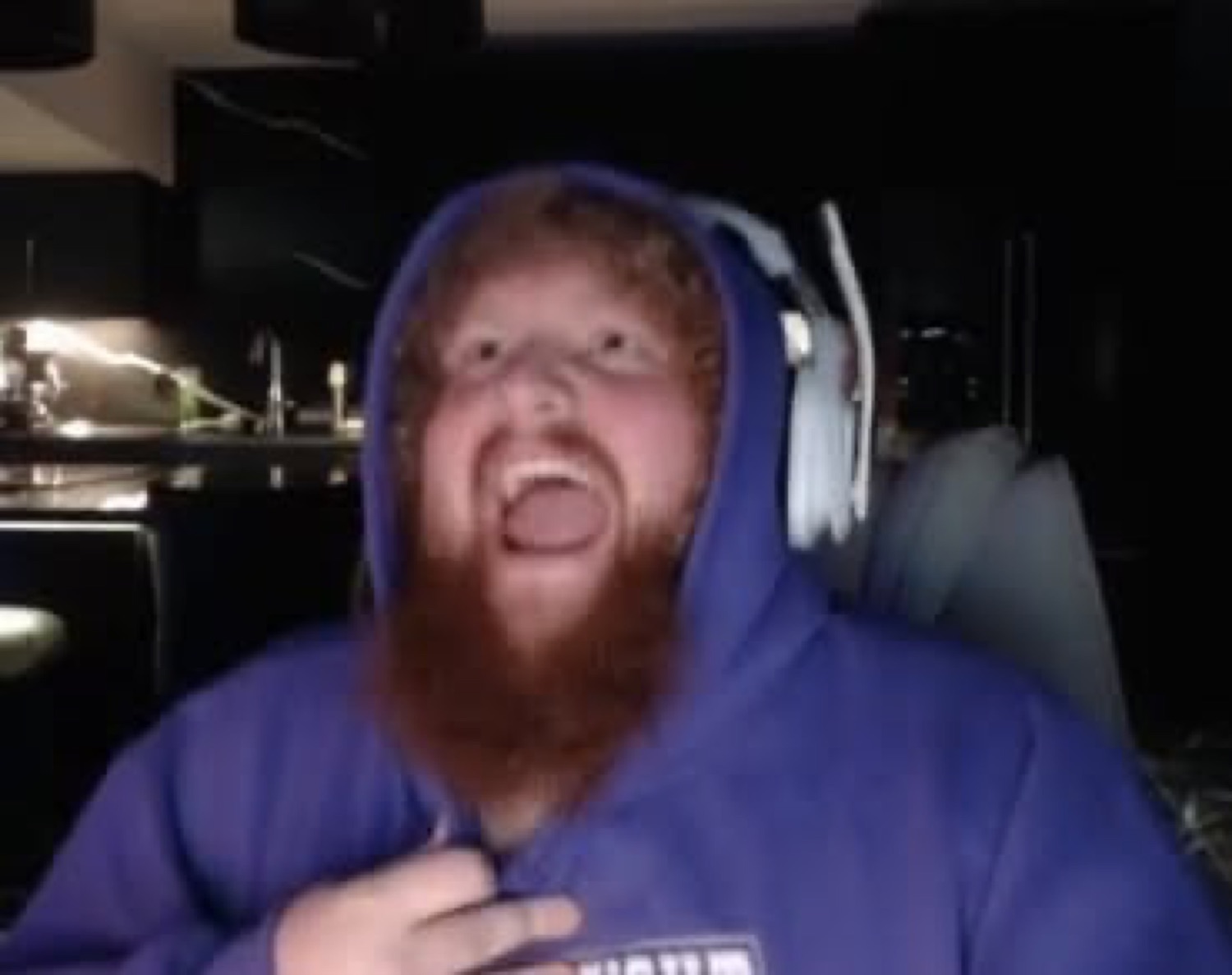 Big bearded gamer in a blue hoodie screaming at his setup with mouth wide open