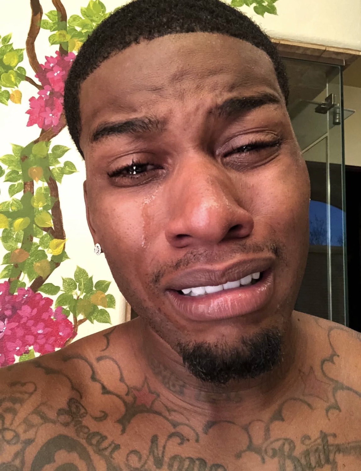 Shirtless man taking a selfie mid-cry with tears streaming down his face
