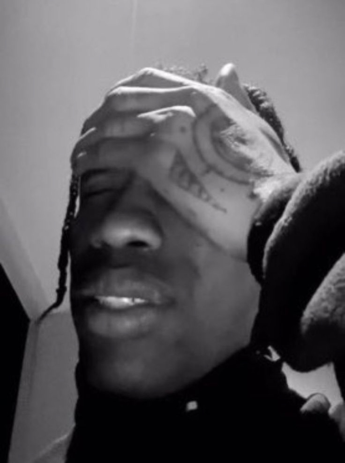 Black-and-white shot of a man with face tattoos smiling and rubbing his forehead