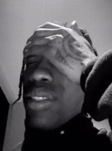 Black-and-white shot of a man with face tattoos smiling and rubbing his forehead