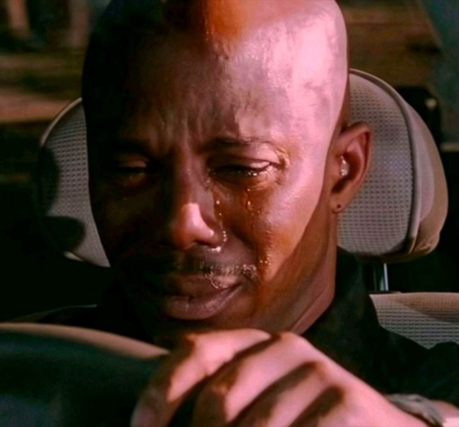 Bald man weeping in a car with his head bowed over the steering wheel