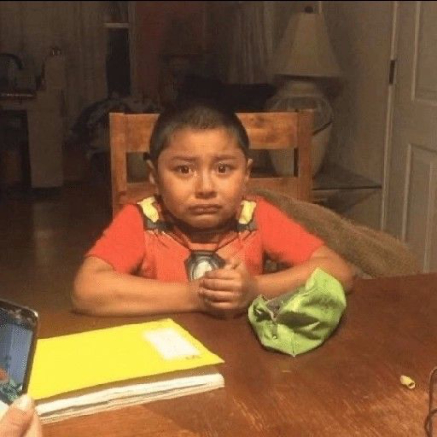 Young kid at a table clutching a drink with a sad, uneasy face
