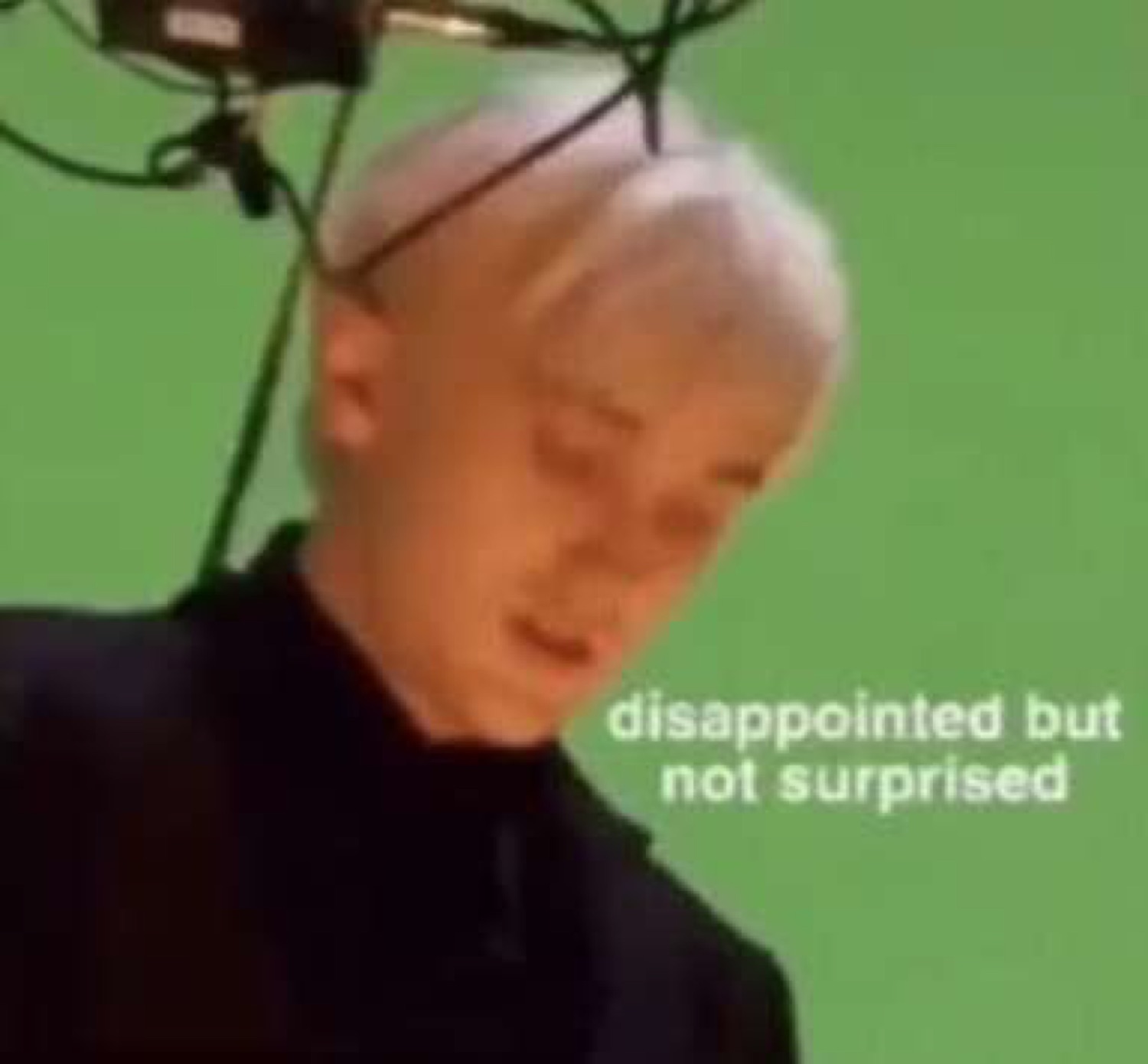 Draco Malfoy on a green screen set looking down under 'disappointed but not surprised'