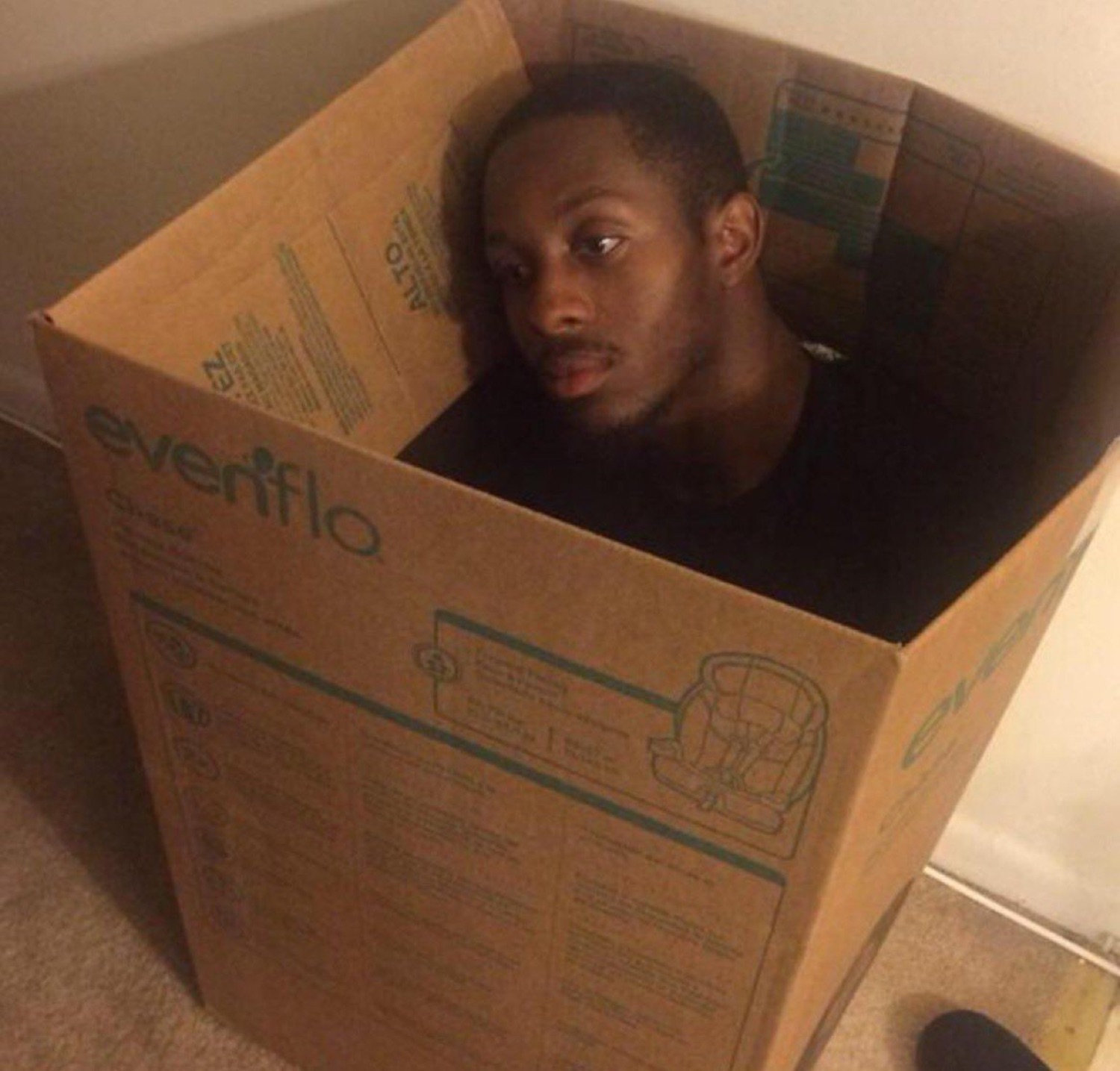 Man sitting inside a cardboard box staring blankly, hiding from the world
