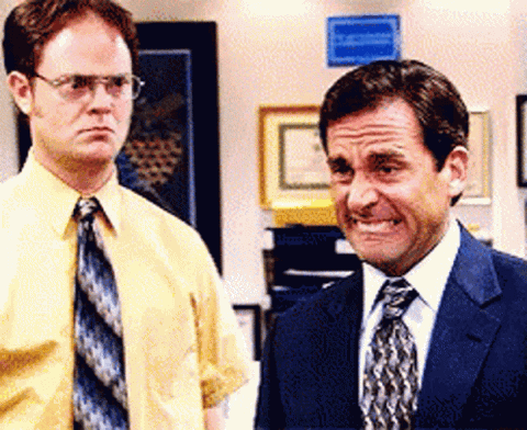 Steve Carell as Michael Scott wincing with clenched teeth, Dwight behind him