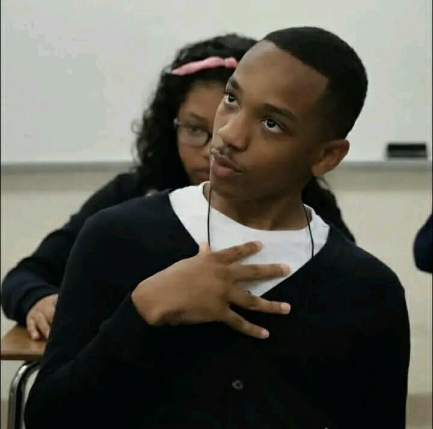 Student with a hand on his chest looking around innocently