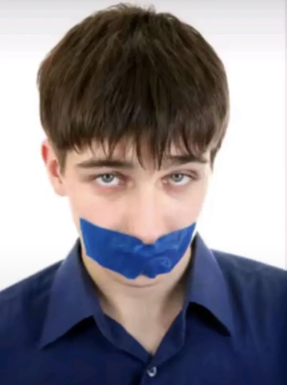 Young man with blue tape over his mouth staring blankly at the camera