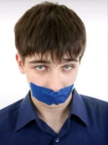 Young man with blue tape over his mouth staring blankly at the camera