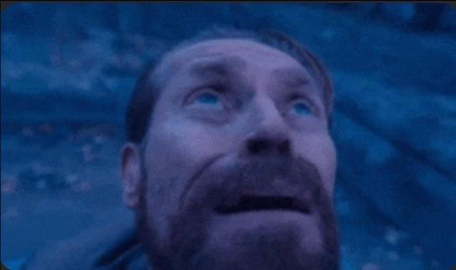 Bearded man lying down and gazing up with wide, teary, awestruck eyes in blue light