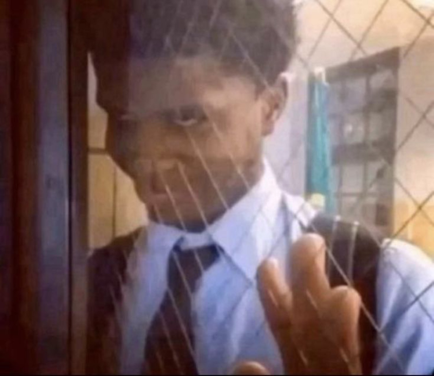Kid in a school uniform peering through a fence with a menacing side-eye