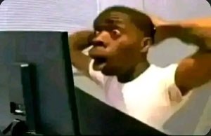 Man clutching his head at a computer monitor, mouth open in shock