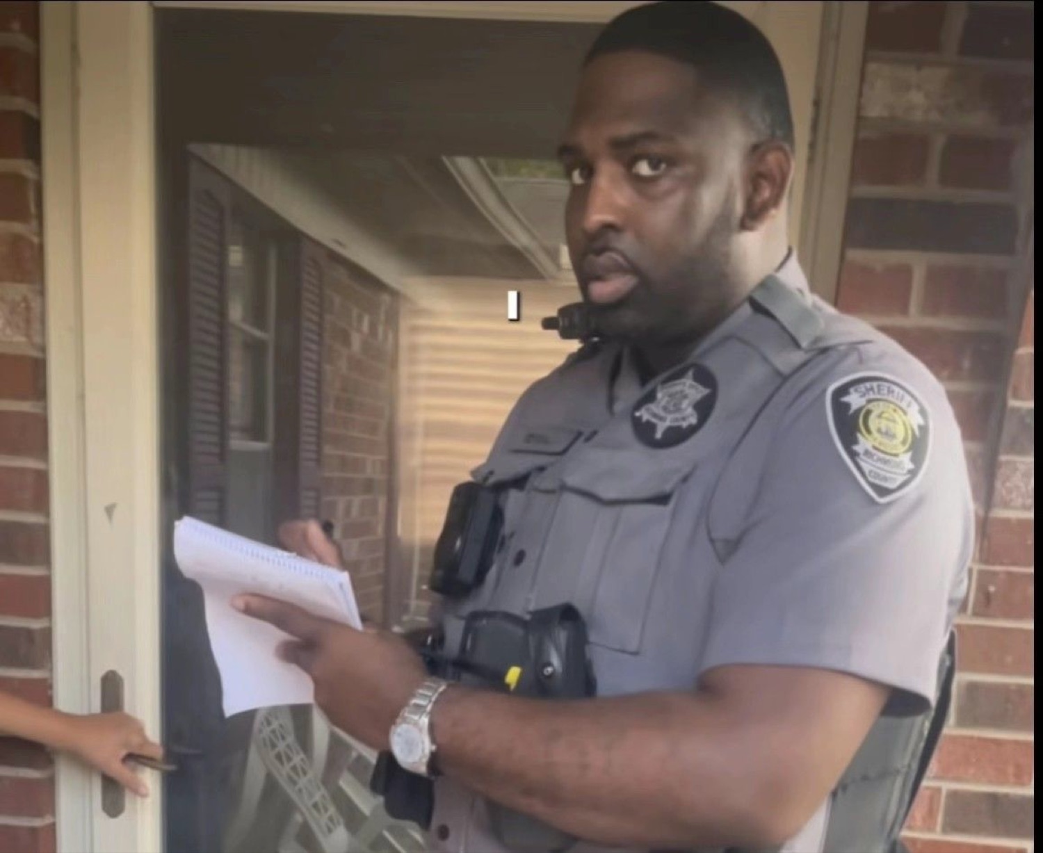 Sheriff's deputy at a doorway giving a skeptical side-eye while holding a notepad