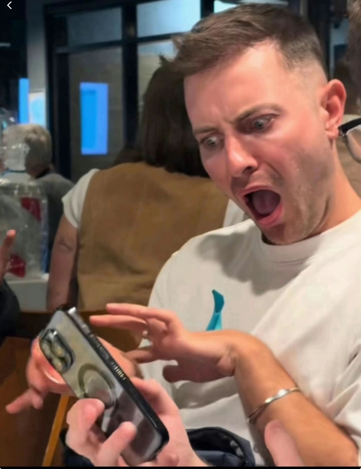 Man at a restaurant table screaming at his phone with his mouth wide open and finger pointing