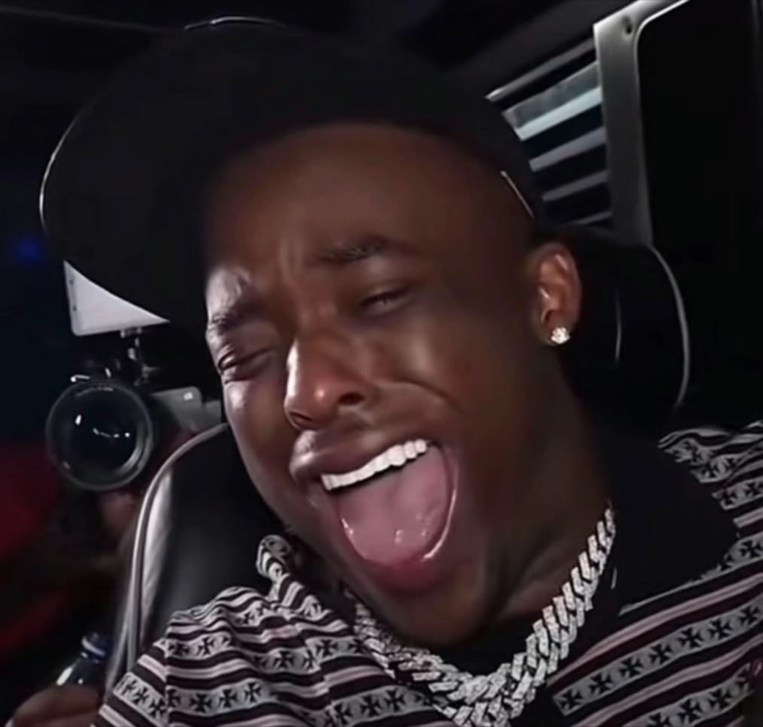 Guy in a backwards cap wailing with his mouth wide open in a car