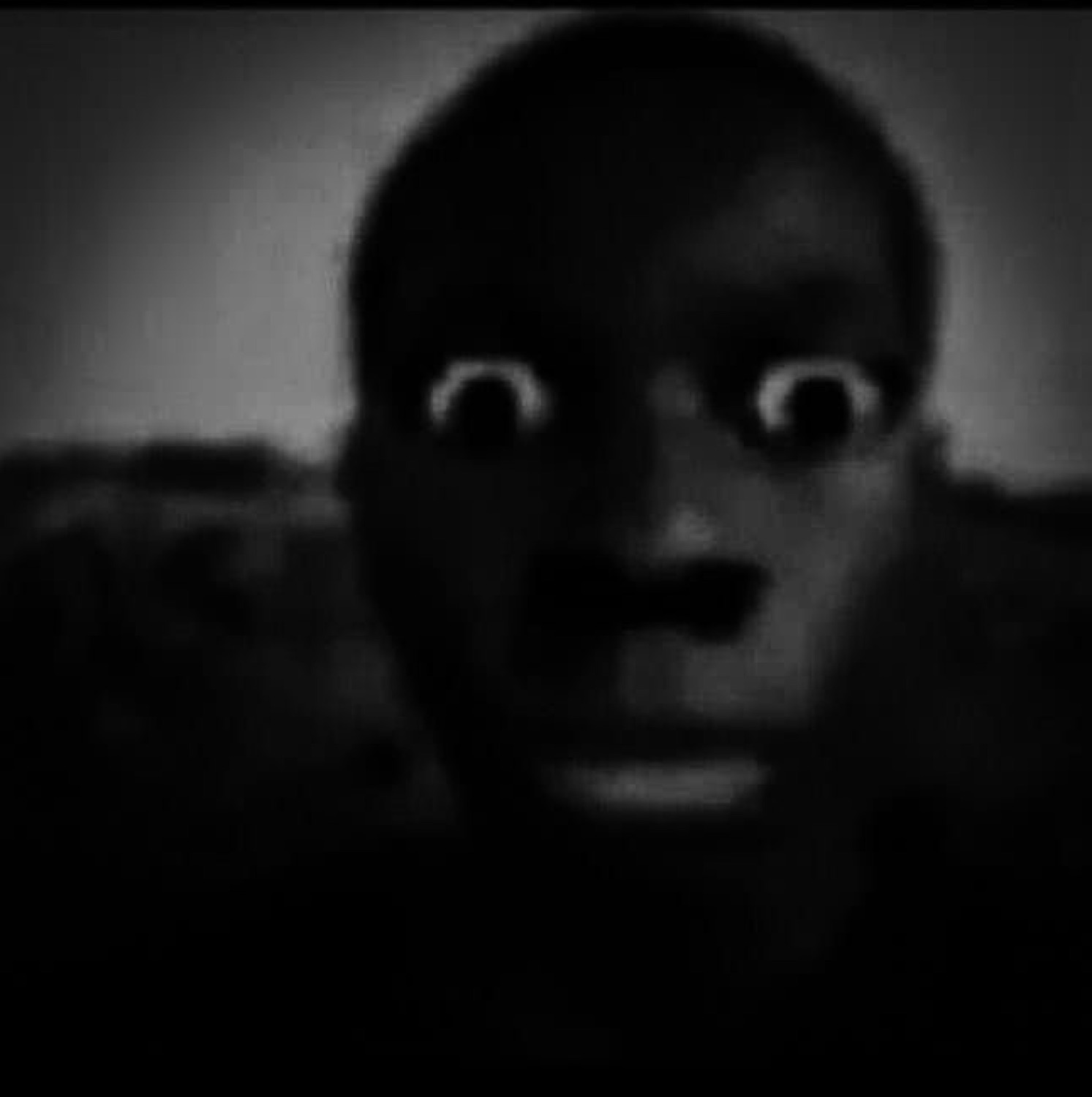 Man staring into the camera in near darkness with huge wide eyes and open mouth