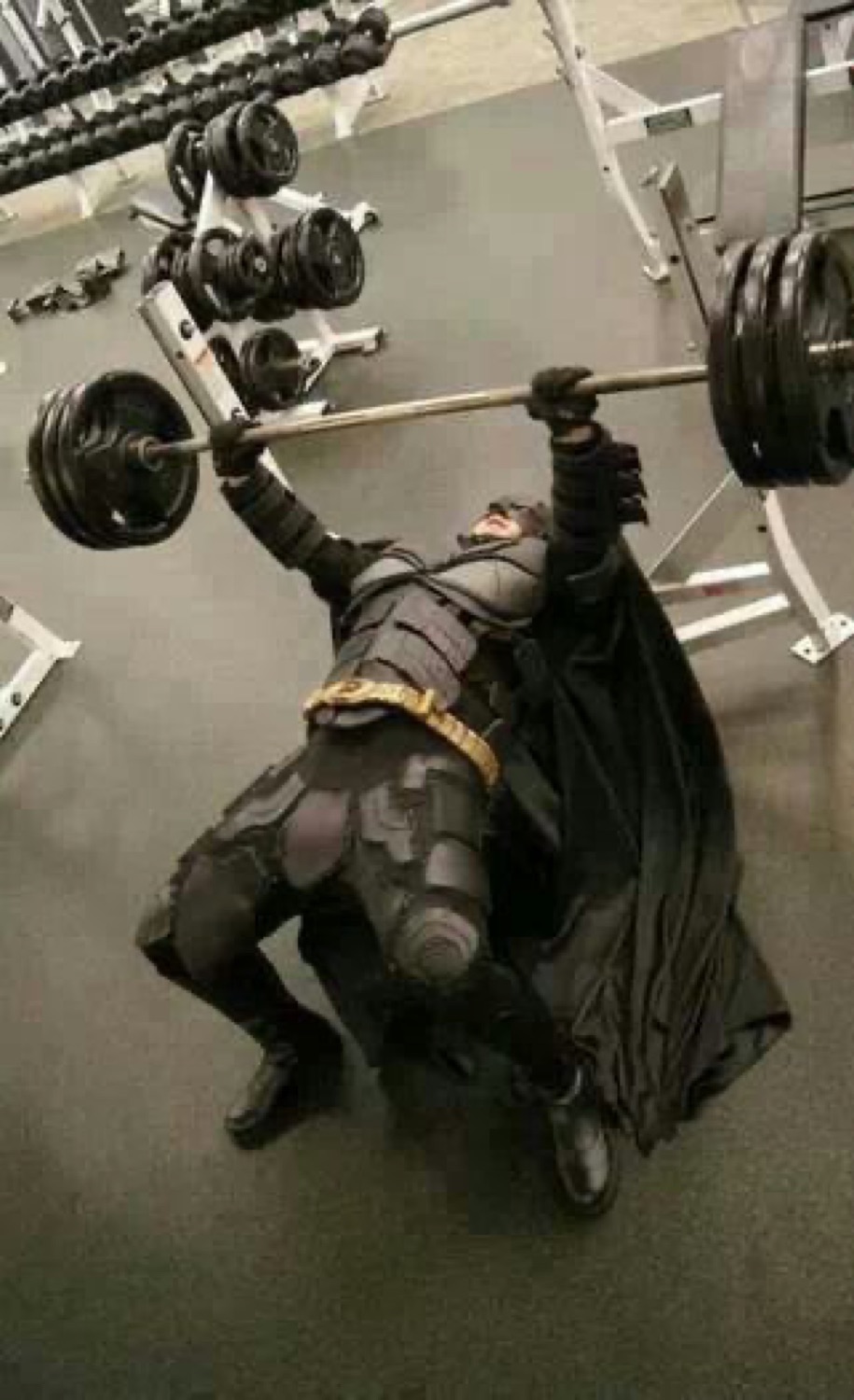 Batman bench-pressing a loaded barbell, seen from above