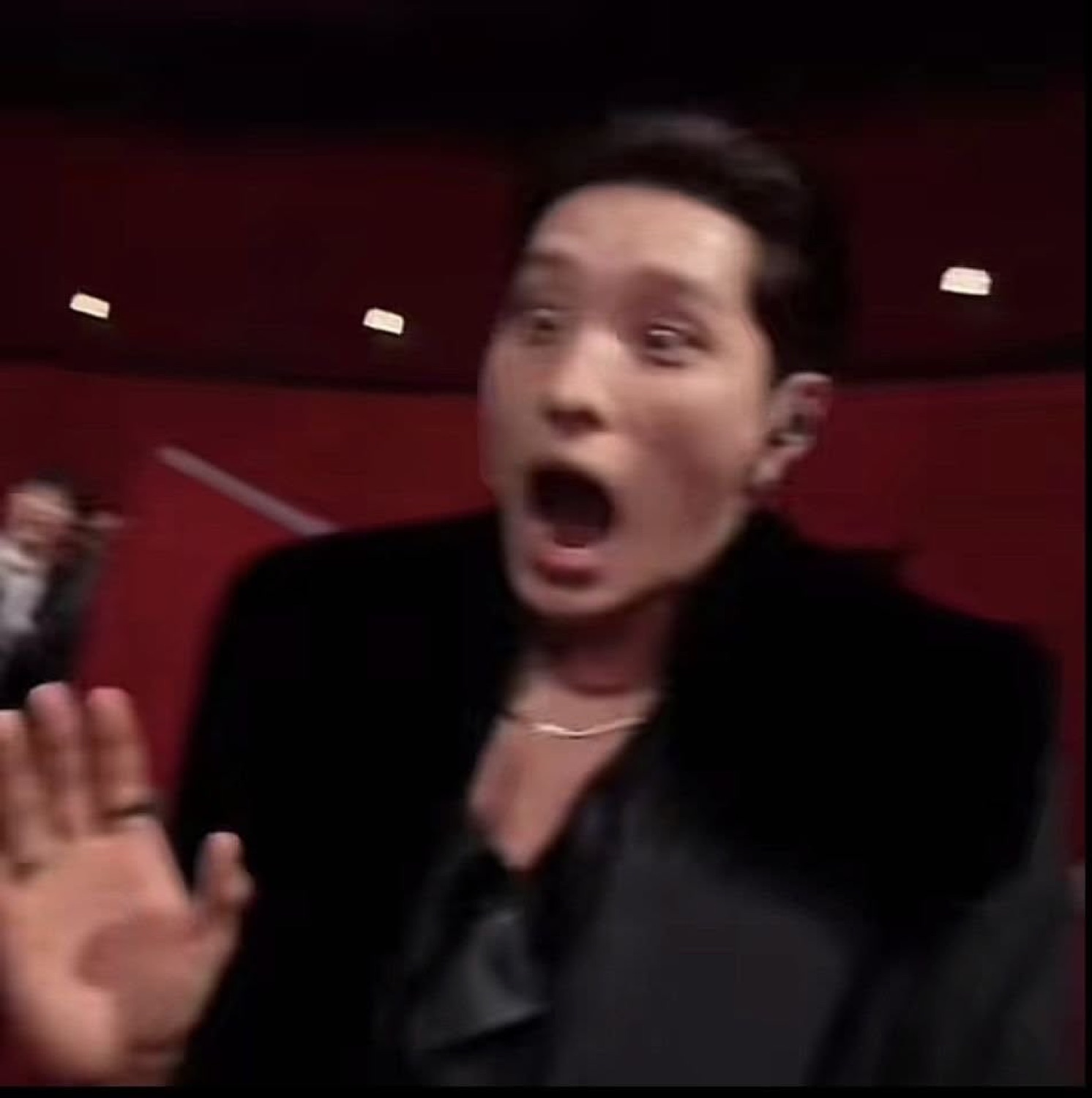 Man in all black recoiling with a wide-open mouth and raised hand in total shock