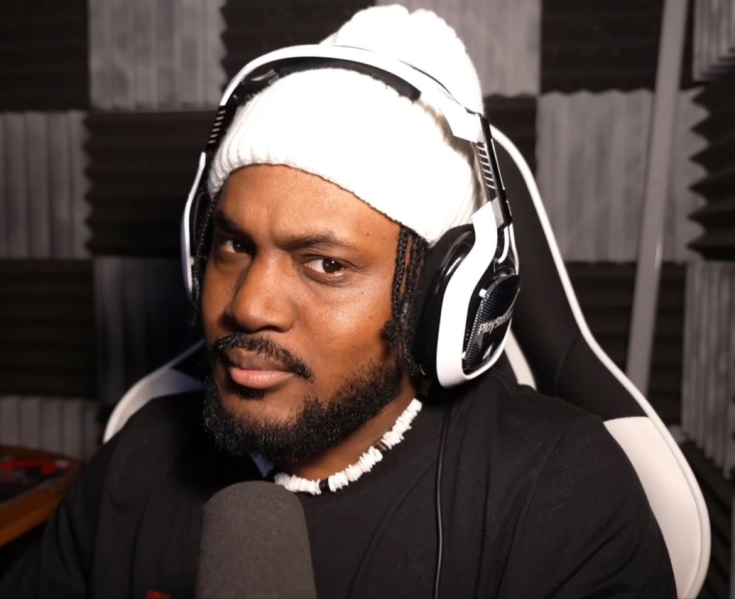 A man in a headset and beanie giving the camera a flat, unimpressed side glance at his mic