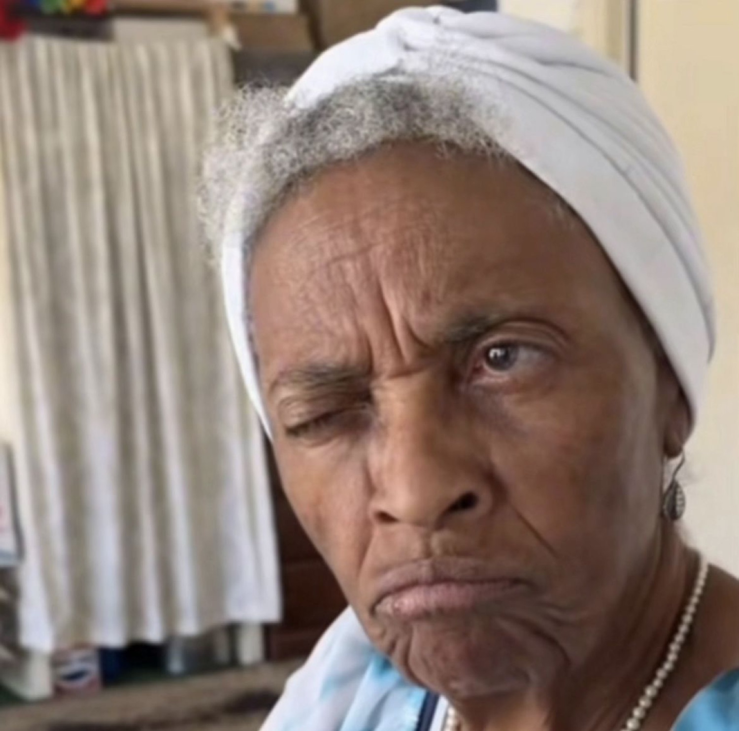 Elderly woman in a head wrap side-eyeing the camera with a full scowl and puffed lip