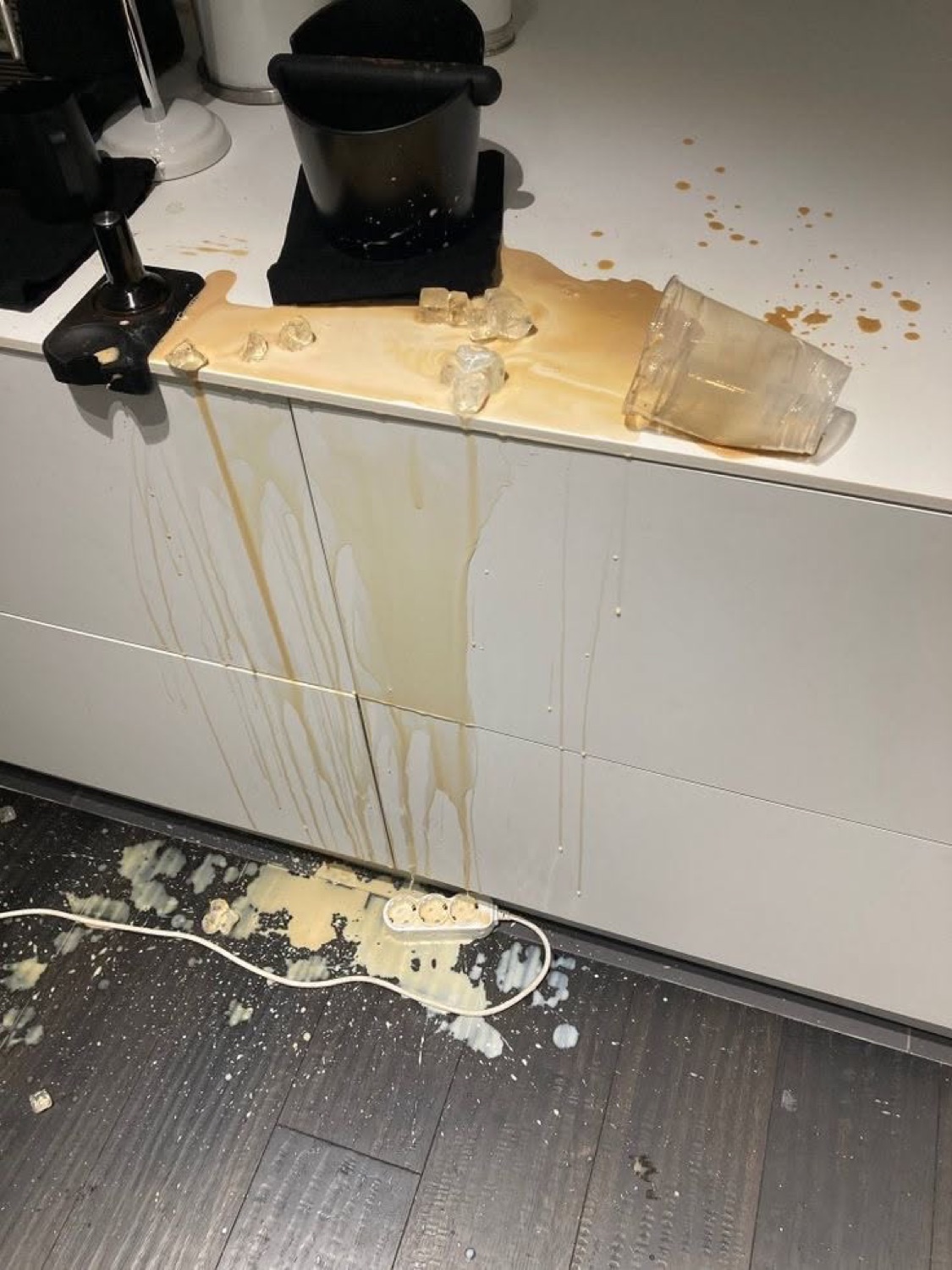 Drink spilled off a white counter with ice and liquid streaming down the cabinet onto the floor