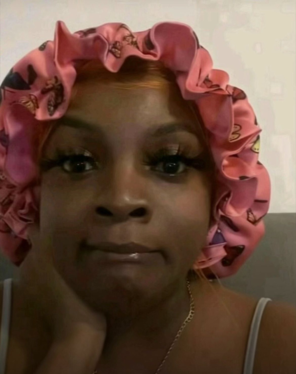 Woman in a pink bonnet resting her chin in her hand with a subtly smug, unbothered look