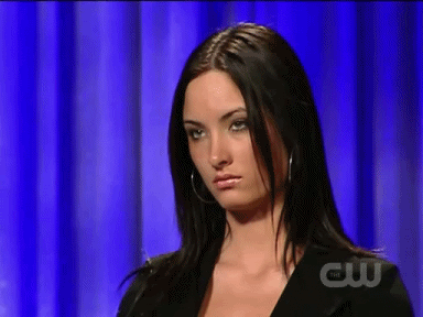 Dark-haired woman on a TV set giving a cold, unimpressed stare against a blue backdrop