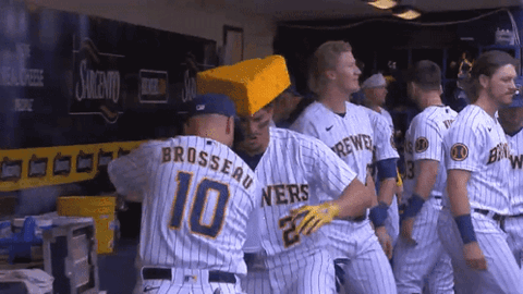 Milwaukee Brewers players celebrating in the dugout, one wearing a cheese hat