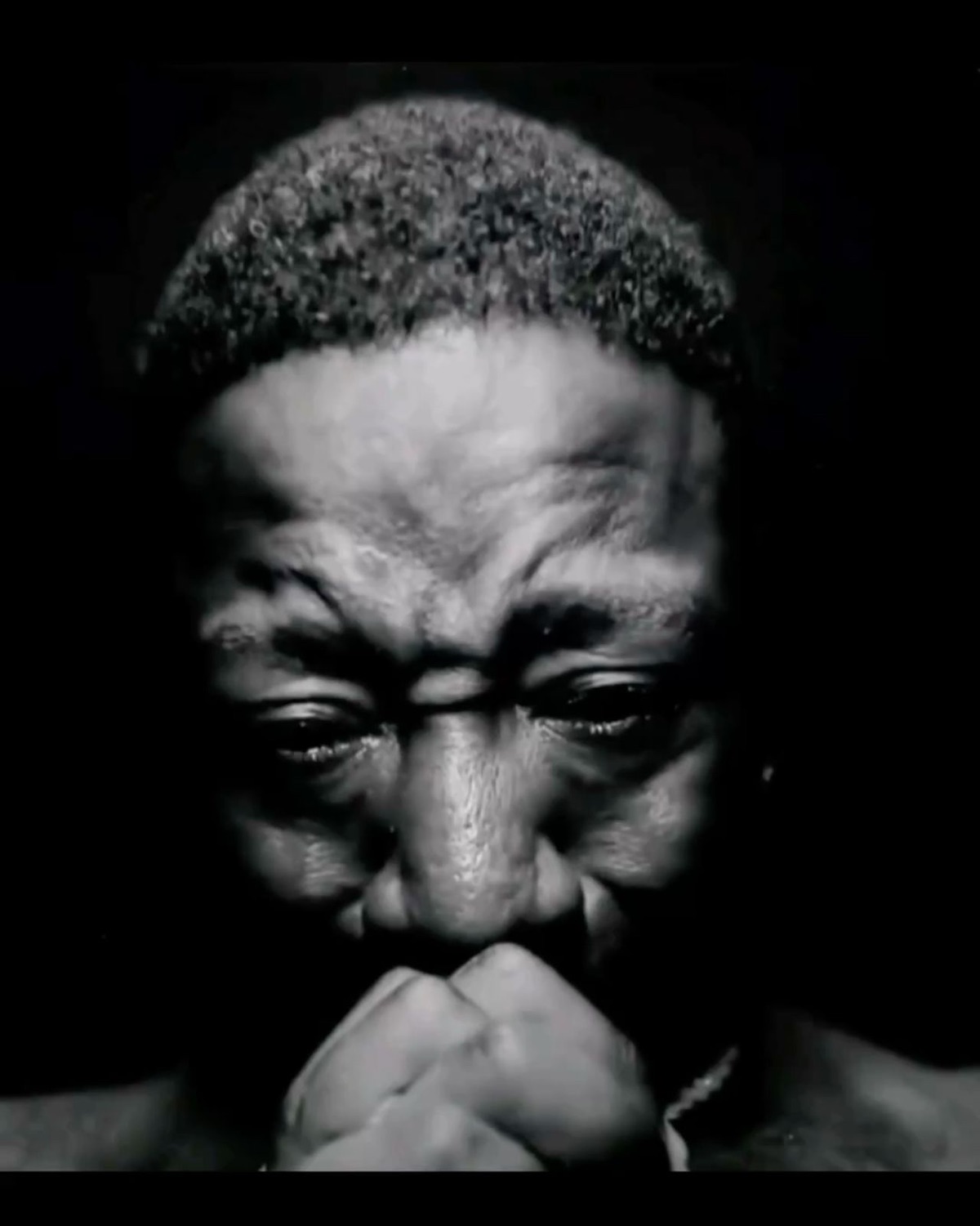 Man in dramatic black-and-white lighting holding back tears with clenched fists at his mouth